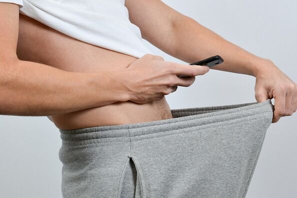 muž sa pozerá cez nohavice na zväčšený penis